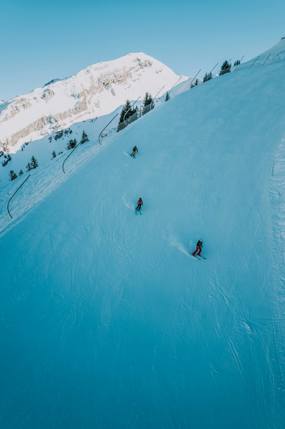 Tre sciatori con giacche colorate scendono un pendio montano innevato.