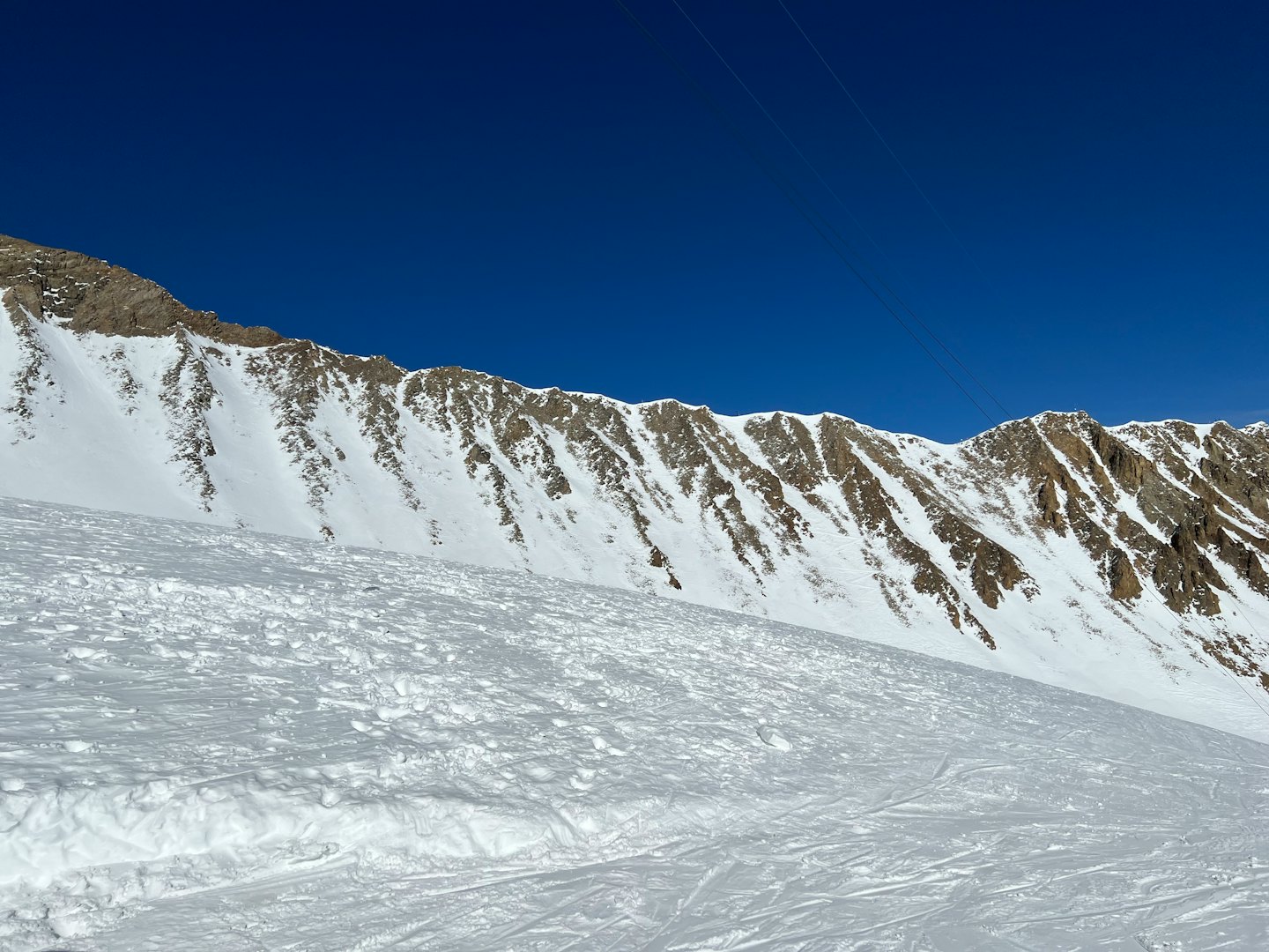 Pendii montuosi innevati con piste da sci sotto un cielo blu.