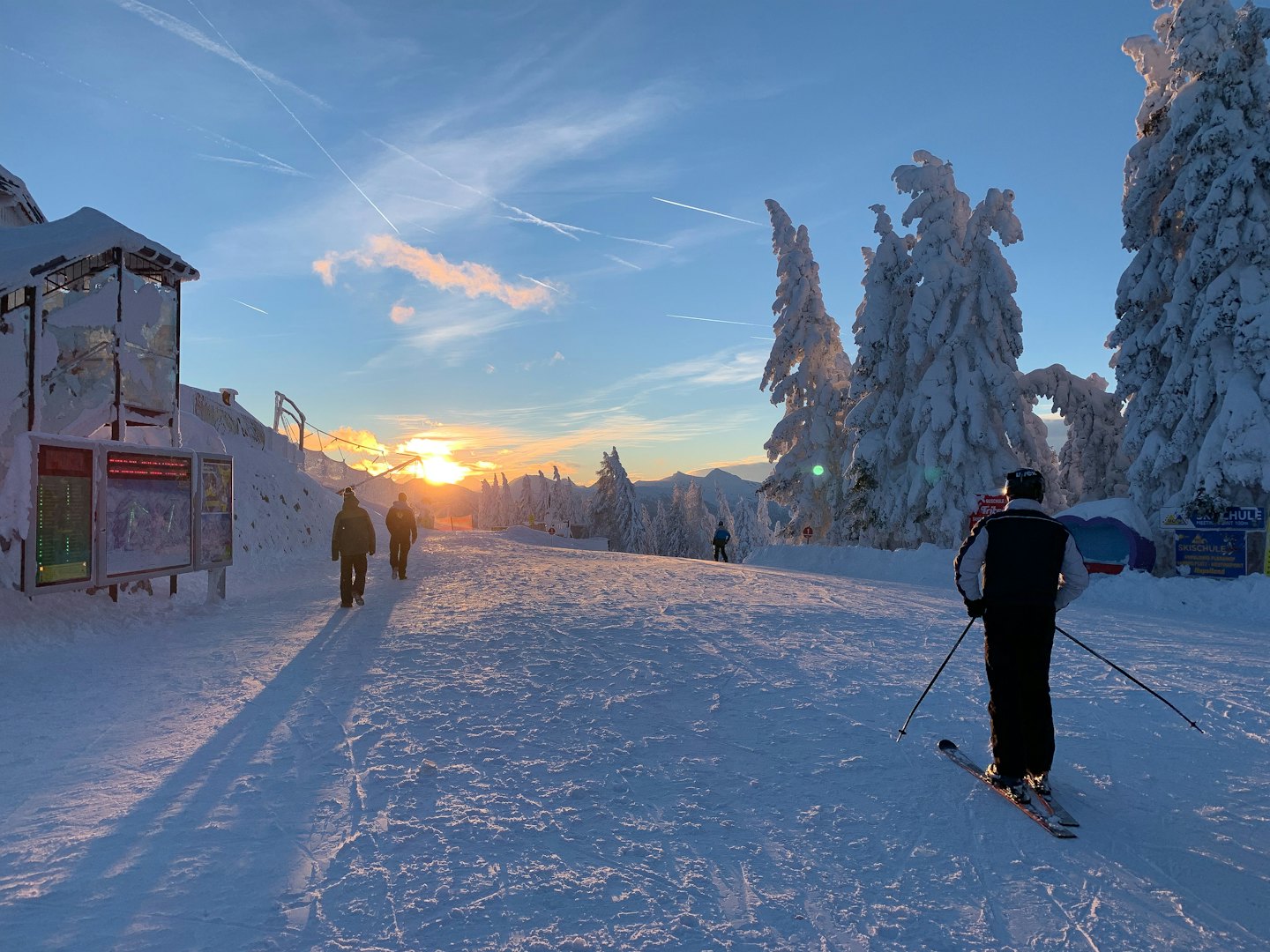 Sciatori su un pendio montuoso innevato al tramonto.