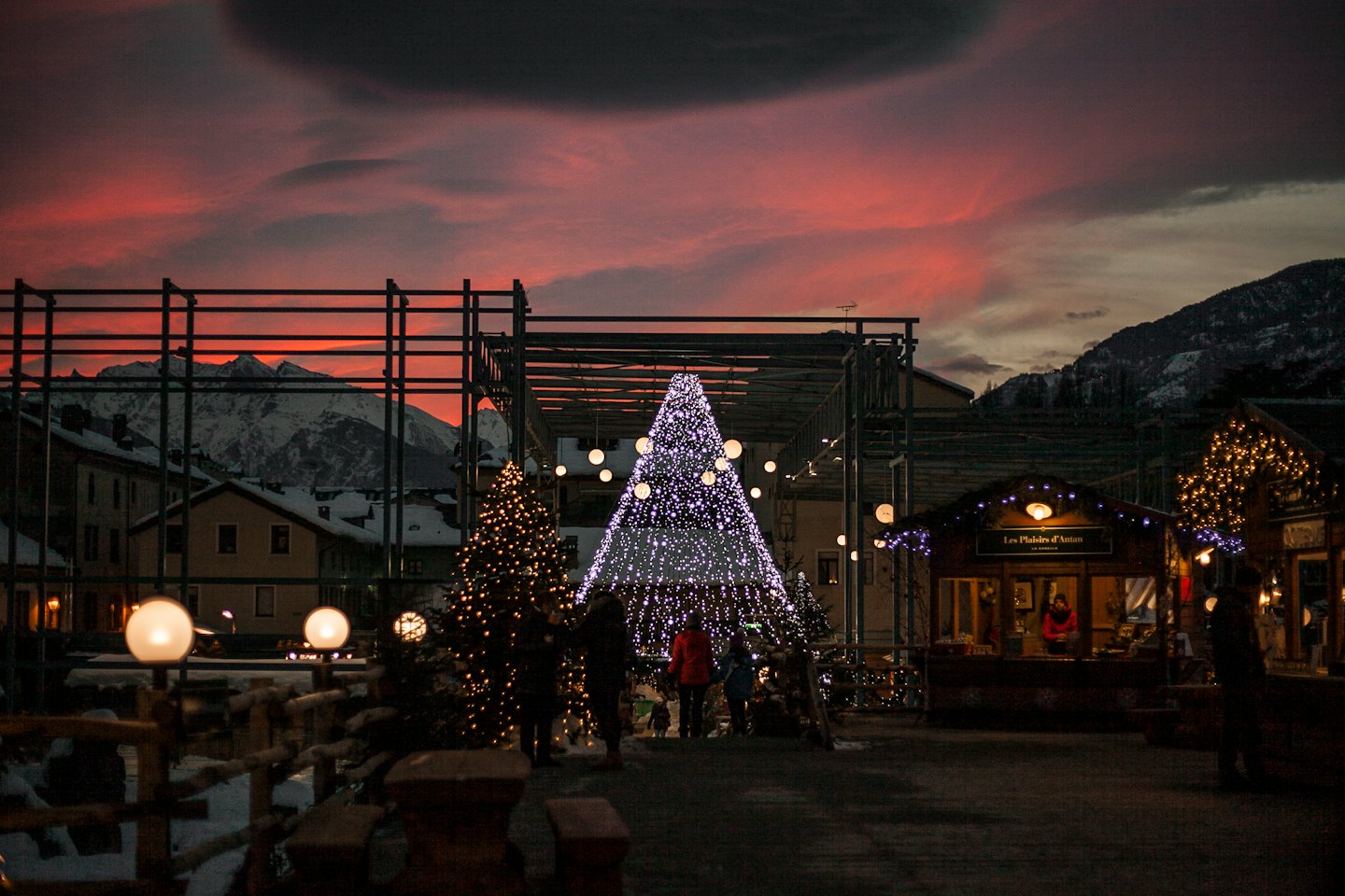 Mercatino di Natale all'aperto con alberi illuminati e bancarelle al tramonto.