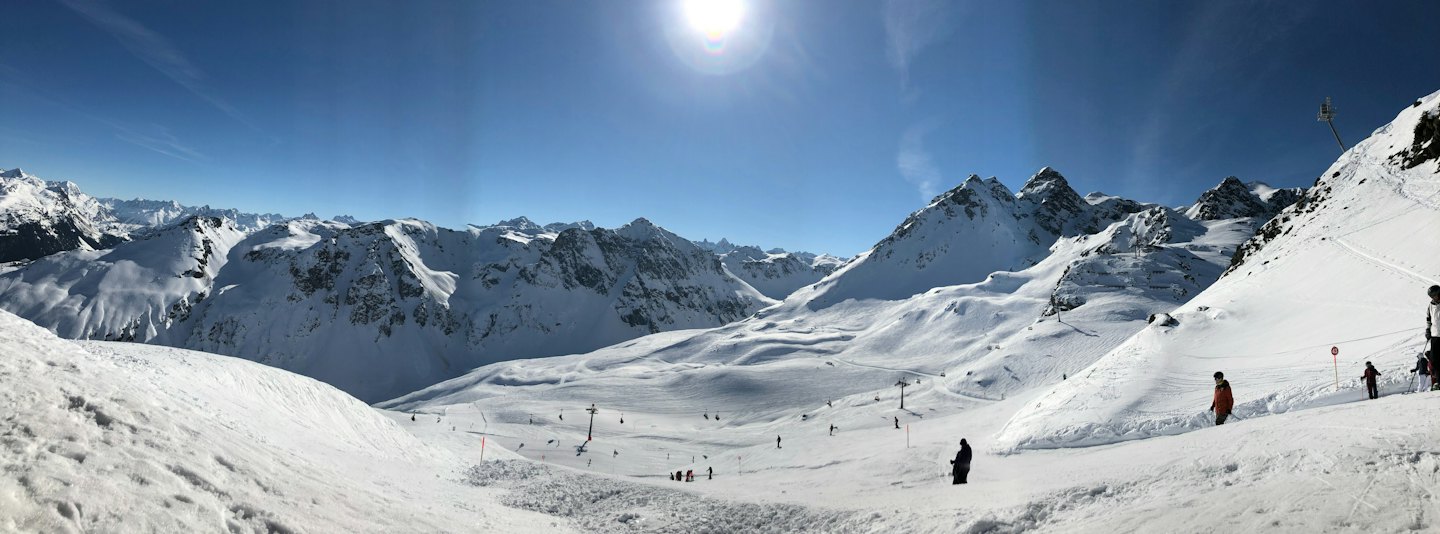 Sciatori sfrecciano su piste innevate in una catena montuosa.