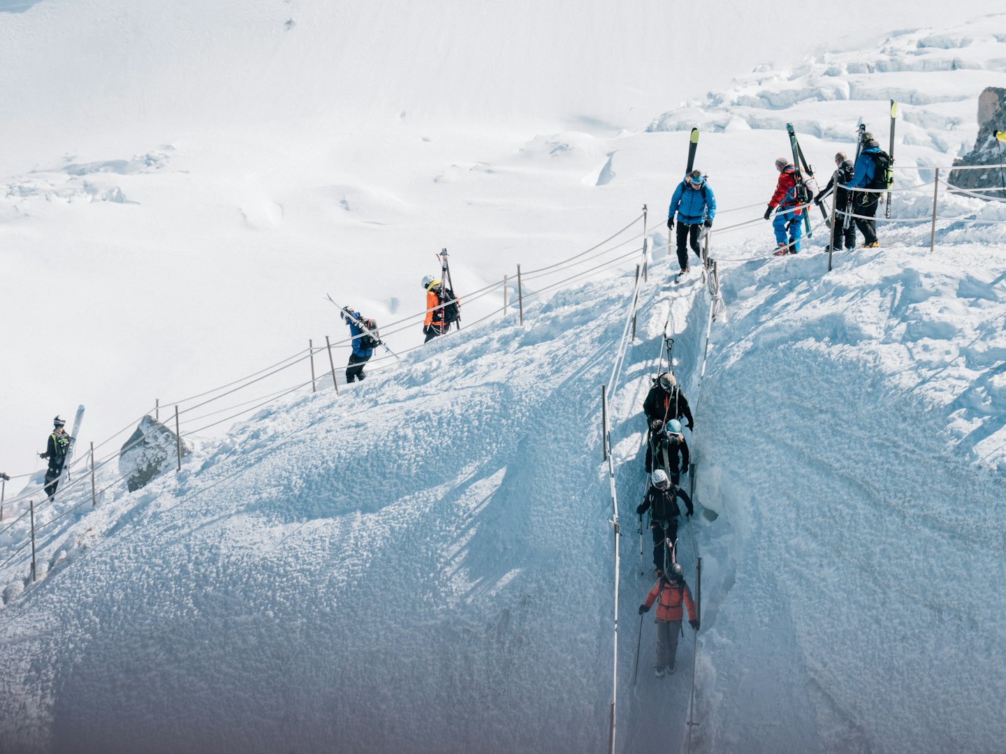 Alpinisti scalano una cresta ripida e innevata usando corde fisse.
